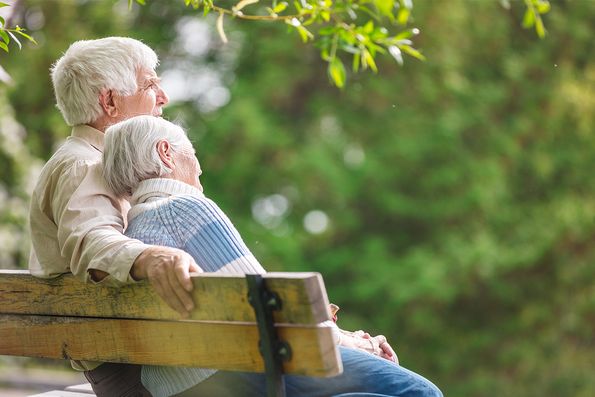 Älteres Paar sitzt auf einer Bank und blickt in die Ferne.